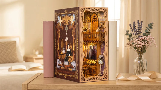 Le book nook Dressing de la Duchesse monté et allumé entre deux livres sur une étagère claire, avec ses robes de bal, à côté d'un vase de fleurs séchées et d'un ruban de cadeau.