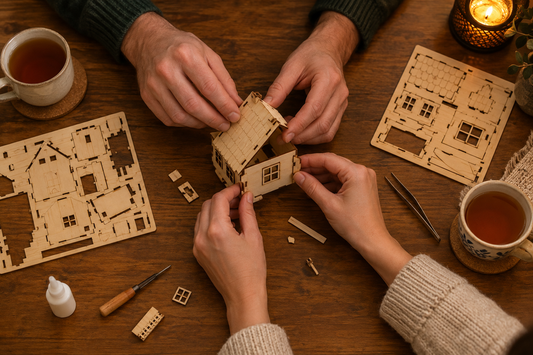 Vue de dessus d’un couple assemblant une maison miniature en bois, avec deux tasses de thé et une lumière chaleureuse.
