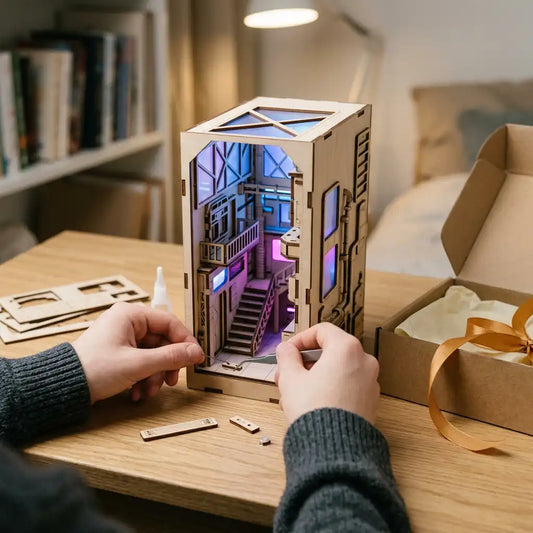 Manos montando un callejón en miniatura con luces azules y magenta, junto a un regalo desenvuelto.