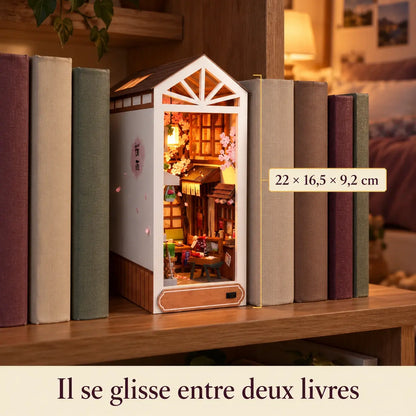 Le book nook Pluie de Sakura glissé entre deux livres sur une étagère, dimensions 22 × 16,5 × 9,2 cm