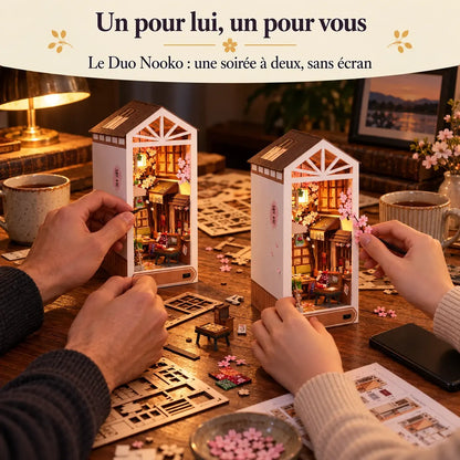 Le Duo Nooko : deux personnes construisent chacune leur maquette Pluie de Sakura à la même table, le téléphone de côté