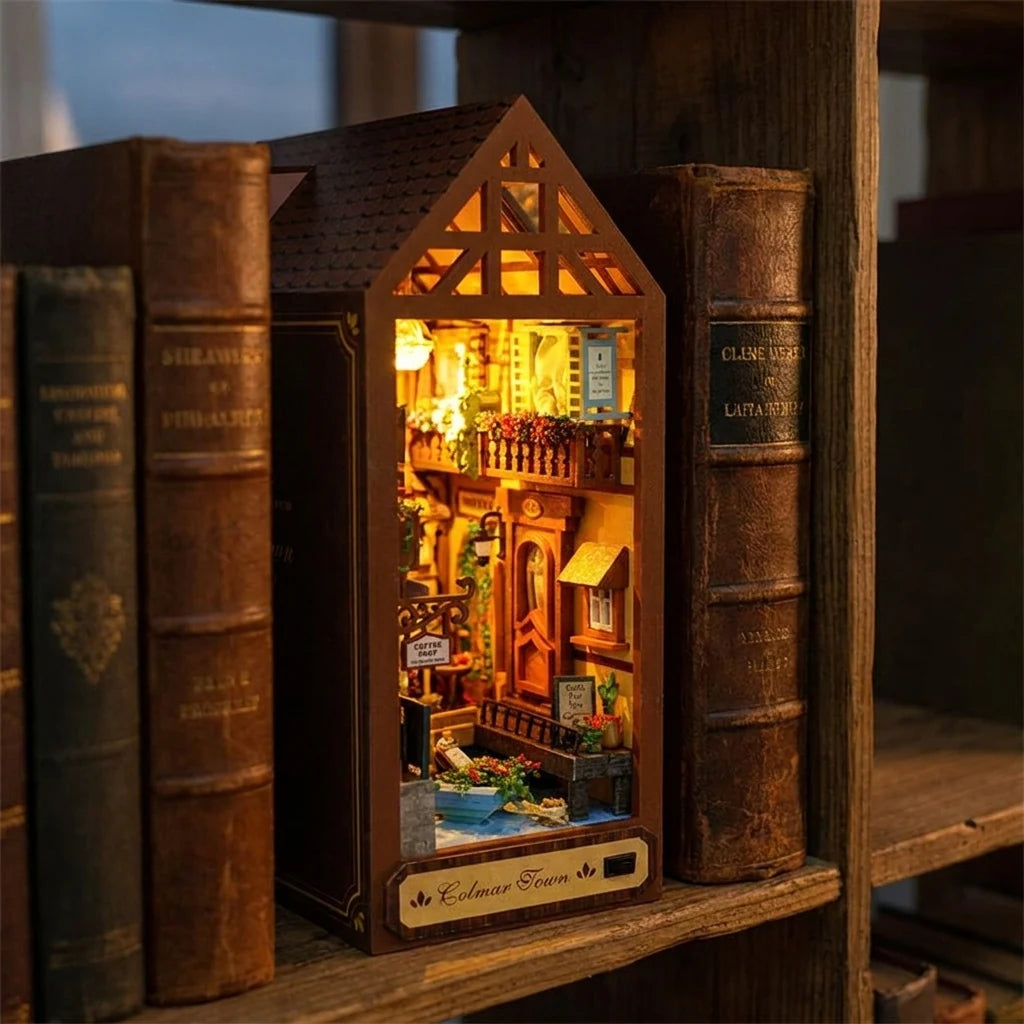 Book nook Maison de Colmar glissé entre deux livres dans une bibliothèque, lumière chaude