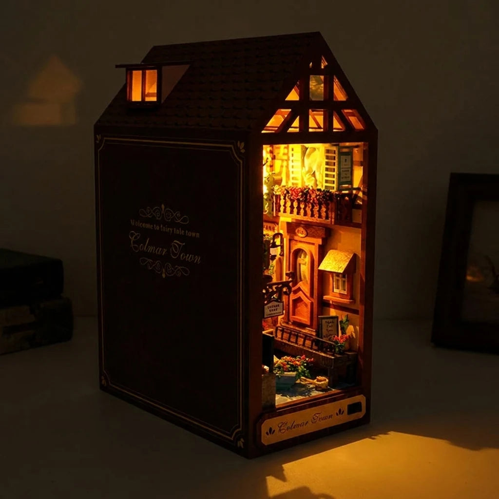 Gros plan du book nook Maison de Colmar, façade alsacienne illuminée la nuit, balcon fleuri