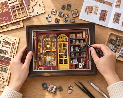 La Librairie du Soir NOOKO — Montage vu du dessus, avec deux mains assemblant les livres miniatures sur une table en bois clair.