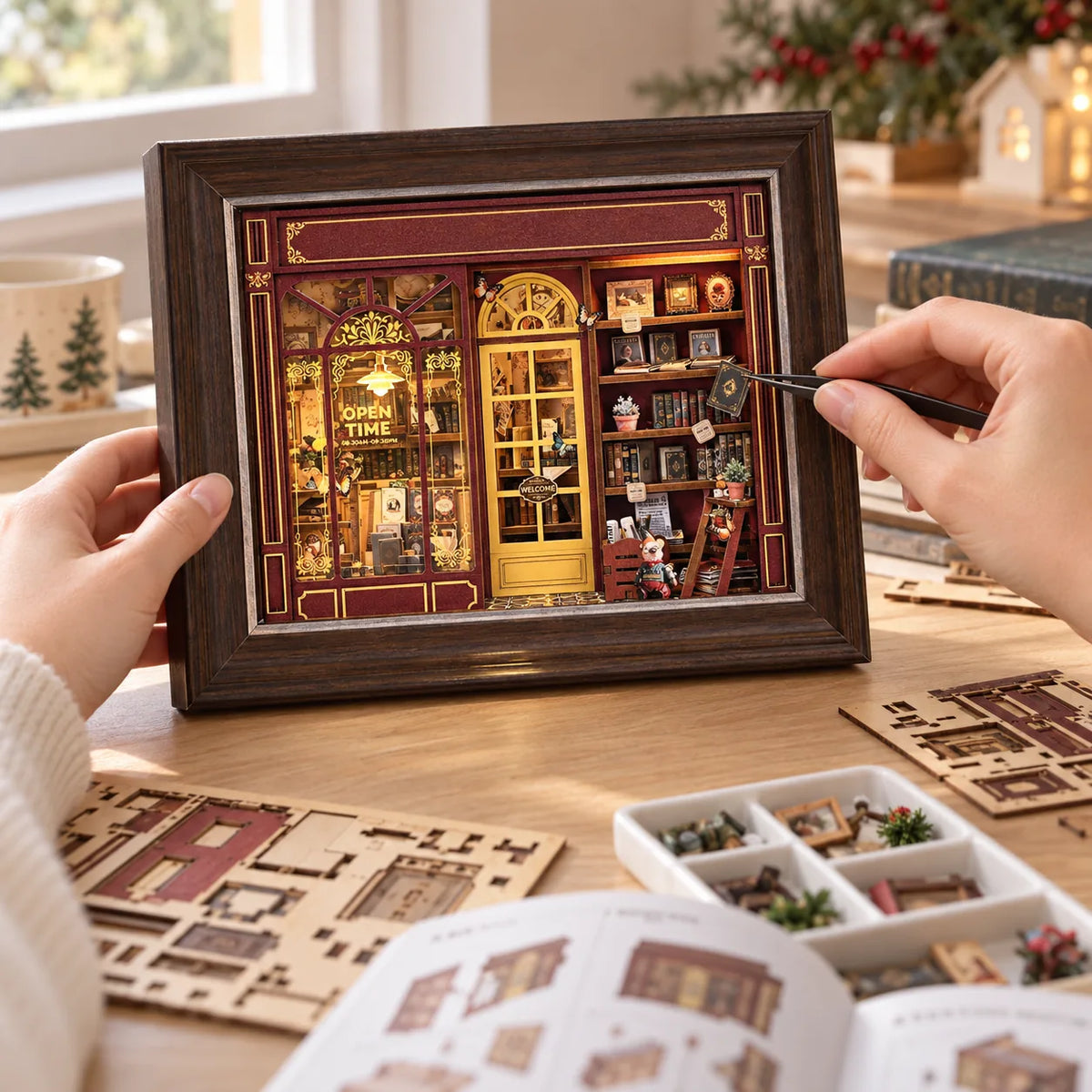 La Librairie du Soir NOOKO — Deux avant-bras assemblent le book nook avec une pince de précision, vu à hauteur de table.