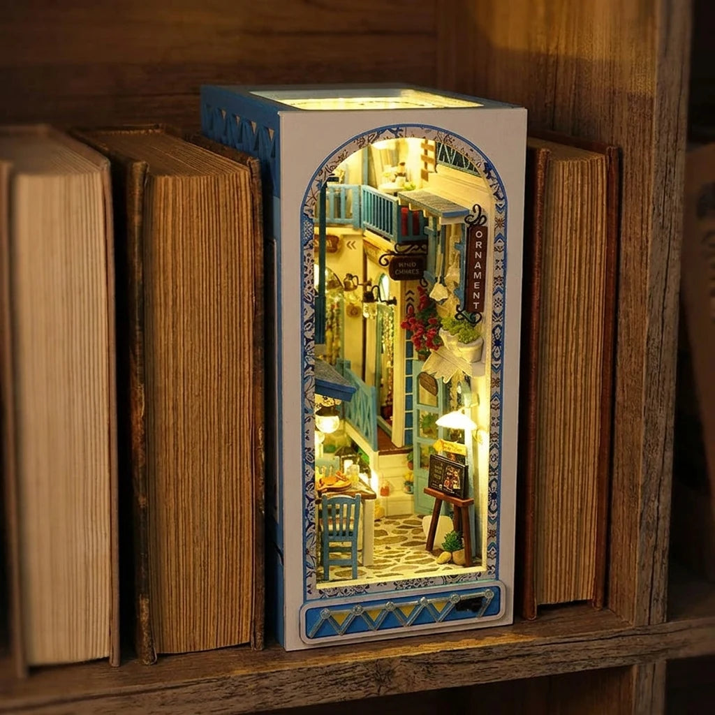 Book nook Ruelle de Santorin glissé entre deux livres dans une bibliothèque, lumière chaude
