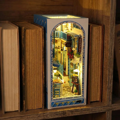 Book nook Ruelle de Santorin glissé entre deux livres dans une bibliothèque, lumière chaude