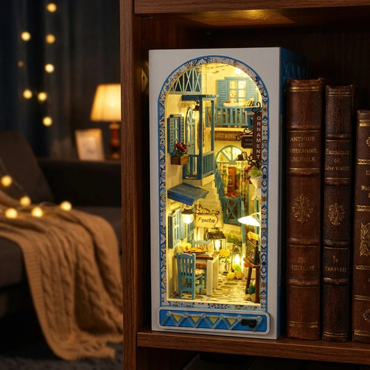 Kit book nook Ruelle de Santorin en bois, façades blanches et volets bleus, posé entre des livres sur une étagère