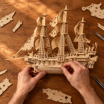 Montage vu du dessus : deux mains assemblent la coque du voilier en bois